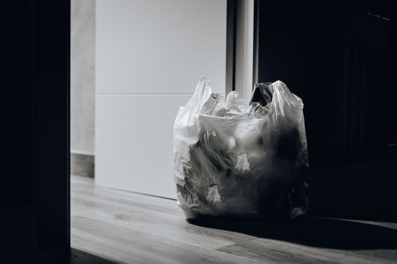 A dimly lit room containing a plastic bag filled with trash, emphasizing waste and recycling.