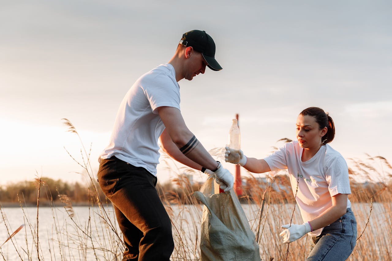 Two volunteers collect trash by a lake at sunset, promoting environmental awareness.